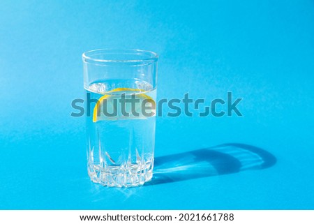 Fresh clean water in a glass with a slice of lemon on a blue background in bright sunlight. Live water, healthy drink