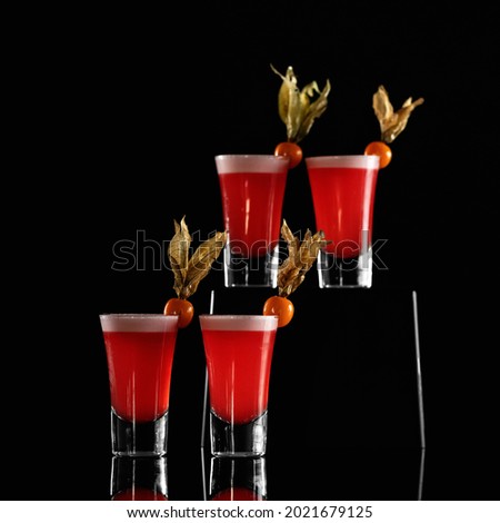 Four glasses with red alcoholic drink decorated with physalis on black background.