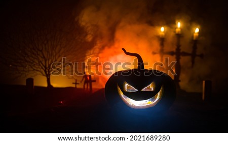 Scary view of zombies at cemetery at night. Dead tree and spooky cloudy sky with fog. Horror Halloween concept with glowing pumpkin. Selective focus