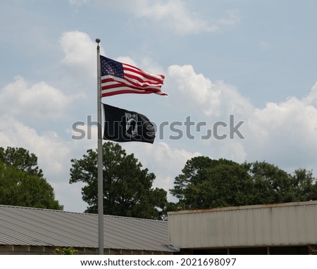 American flag flowing with POW flag underneath on flagpole on windy day near a building