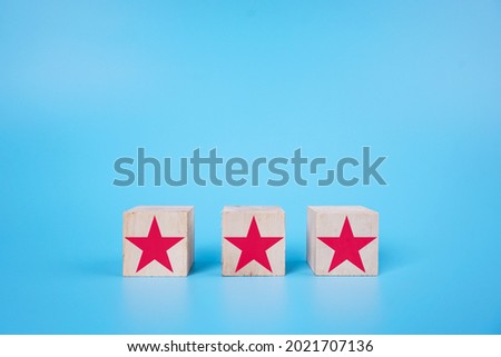 Three Red Star symbol on a wooden cube over blue background. Evaluate, ranking concept
