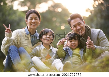happy asian family with two children having good time sitting on grass in city park