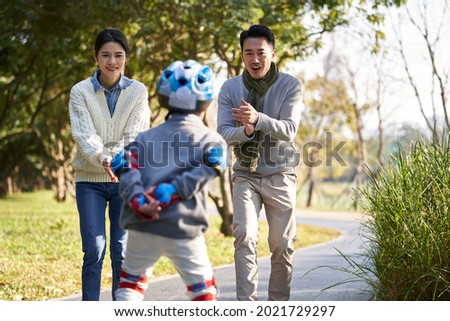 loving asian parents teaching son roller skating outdoors in city park