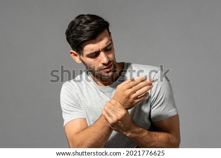Young Caucasian man having wrist pain, studio shot in isolated gray background