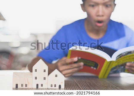 Asian man shows amazement while looking at a book, small wooden house model, home buying planning