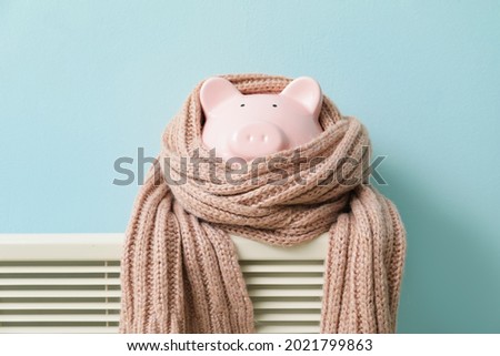 Piggy bank with scarf on radiator. Concept of heating season