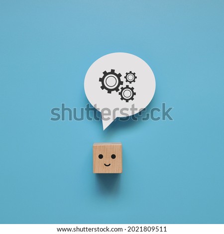 A wooden cube with a smile and a picture of gears above it. A symbol of brainstorming and reflection