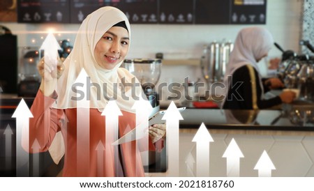 Asian muslim businesswoman pointing arrow up of future business growth graph plan or chart financial goals with coffee shop counter background