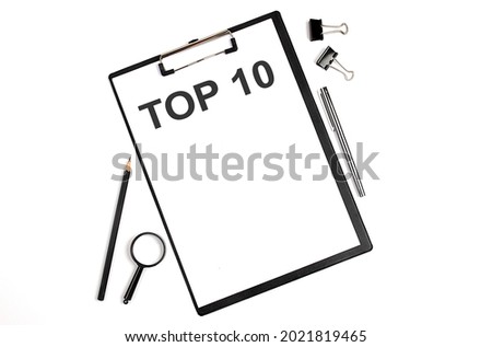 On a white background magnifier, a pen and a sheet of paper with the text TOP 10 , . Business