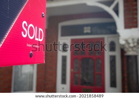 Estate agent SOLD sign with blurred house door in background