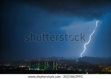 A huge lightning strikes the mountain in the night. Thunderstorm over the city. Deafening Thunder. Raindrops glow at night. Matte, dramatic picture with low sharpness.