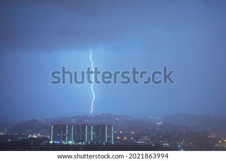 A huge lightning strikes the mountain in the night. Thunderstorm over the city. Deafening Thunder. Raindrops glow at night. Matte, dramatic picture with low sharpness.