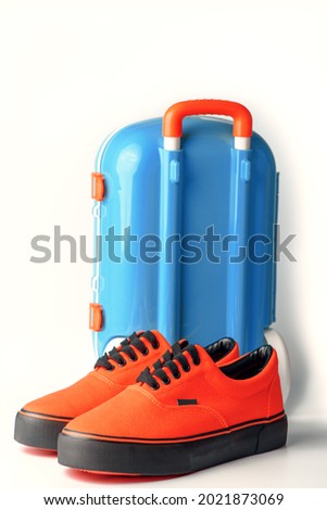 Blue suitcase and orange gumshoes on white background. Travel concept. Copy space