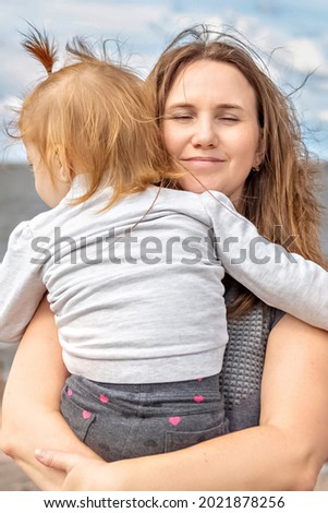 Mom with a little daughter in her arms hugging on the beach.