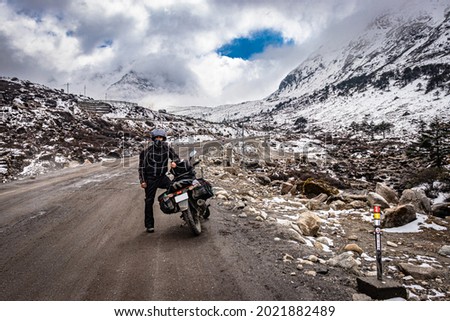 man solo ridder in ridding gears with loaded motorcycle at isolated road and snow cap mountains image is taken at sela pass tawang arunachal pradesh. Royalty-Free Stock Photo #2021882489