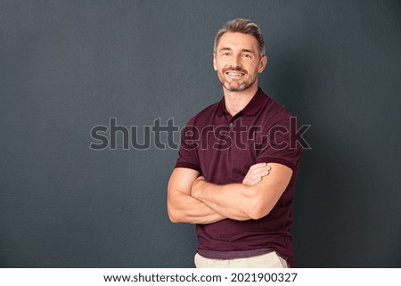 Portrait of smiling mature man standing on gray wall with folded arms. Successful mid adult man with folded arms standing over grey background while looking at camera with copy space. Royalty-Free Stock Photo #2021900327