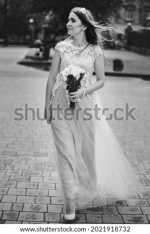 Beautiful happy bride in stylish vintage dress walking in sunny street on background of church. Emotional smiling bride walking with wedding bouquet of roses and lavender. Provence wedding