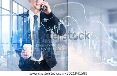 Businessman wearing formal suit is standing at the workplace inside an office drinking coffee and talking via smartphone. Forex candlesticks and graph in the foreground. Concept of communication