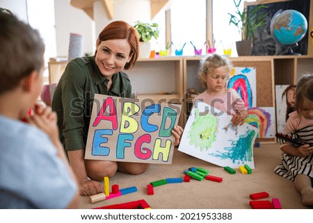 Group of small nursery school children with teacher on floor indoors in classroom, learning. Royalty-Free Stock Photo #2021953388