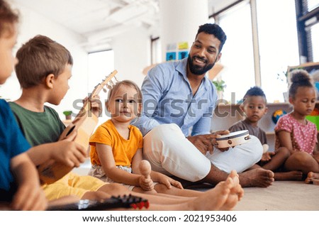 Group of small nursery school children with man teacher sitting on floor indoors in classroom, playing. Royalty-Free Stock Photo #2021953406