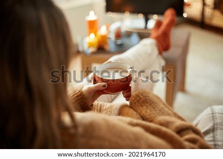 halloween, holidays and leisure concept - close up of young woman watching tv and drinking hot chocolate with her feet on table at cozy home
