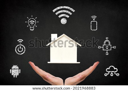 Smart home systems, hands holding a wooden house with smart home icons on blackboard