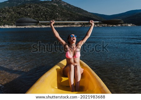 happy caucasian woman holding oar sitting on yellow canoe in lake during sunny day. summer time. Sports, adventure and nature
