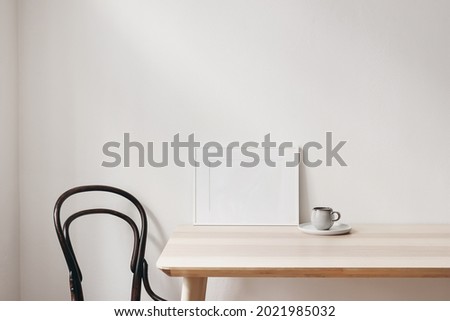 Breakfast still life scene. Cup of coffee, books and empty horizontal white picture frame mockup on wooden table. Elegant working space, home office concept. Scandinavian interior design. Living room. Royalty-Free Stock Photo #2021985032