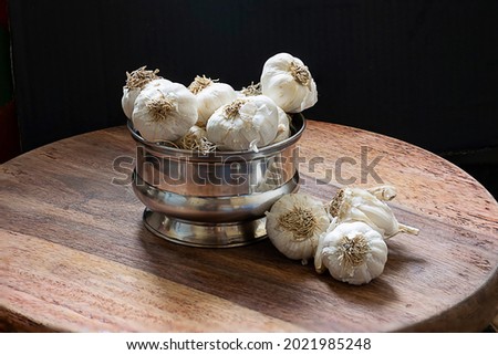 Stock photo of bunch of unpeeled raw medium size Indian garlic kept on steel container on brown wooden table on black background.