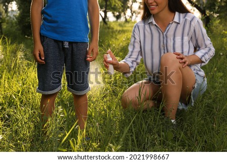Woman applying insect repellent on her son's leg in park, closeup. Tick bites prevention