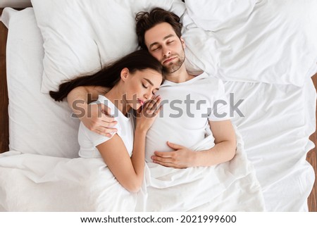 Married Couple Sleeping Together Embracing Lying In Comfortable Bed At Home At Night. Top View Shot Of Spouses Resting Peacefull Enjoying Nap In Comfortable Bedroom Royalty-Free Stock Photo #2021999600