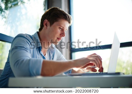 Caucasian male freelancer using laptop application for working remotely during daytime, skilled man browsing wireless website connecting to public internet for doing web projecting on netbook
