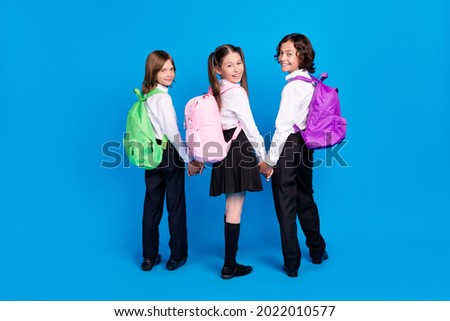 Photo of pretty adorable schoolchildren wear uniform rucksacks holding arms walking smiling isolated blue color background