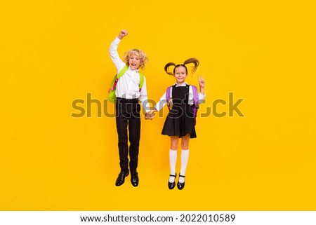 Photo of crazy children jump hold hands show victory sign wear school uniform isolated yellow color background