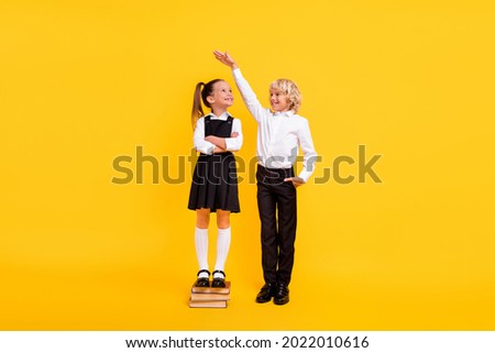 Photo of confident kids girl stay pile book boy measure height wear school uniform isolated yellow color background