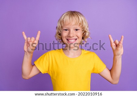 Photo of positive funky blonde kid rocker fan boy toothy smile wear yellow t-shirt isolated violet color background Royalty-Free Stock Photo #2022010916