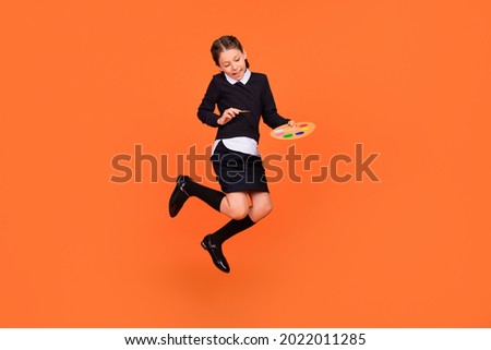 Full length body size view of pretty cheerful preteen girl jumping drawing design craft isolated over bright orange color background