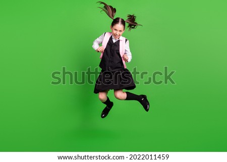 Photo of carefree positive schoolgirl dressed white black uniform rucksack smiling jumping high isolated green color background