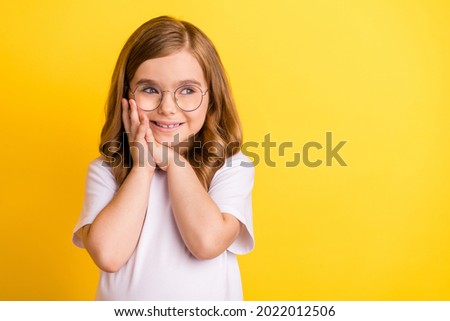 Photo of impressed pretty school girl wear white t-shirt spectacles smiling looking empty space isolated yellow color background