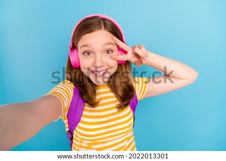 Photo of cheerful redhair schoolgirl make selfie fingers show v-sign near eye isolated on blue color background
