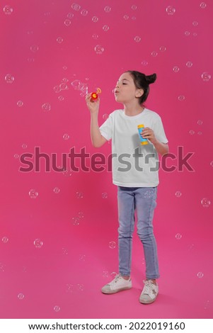 Little girl blowing soap bubbles on pink background