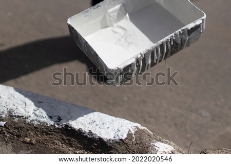 Painting borders with white paint. Applying oil paint to asphalt. Creation of markings for pedestrians. Paint brush. Work as a painter. Painting the surface with a thick layer of paint.