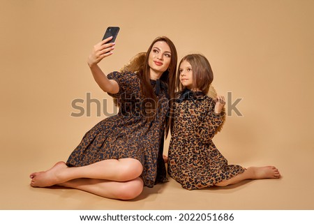 Two beautiful young girls sisters take selfies in nice animal pattern dresses with straw hats posing in studio.
