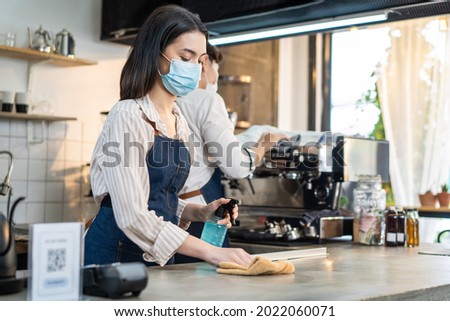Cafe waiter wear mask, clean restaurant with sanitizer to open store. Asian attrctive young couple disinfecting, wiping and rubbing on counter in restaurant before reopen store after Covid19 lockdown. Royalty-Free Stock Photo #2022060071