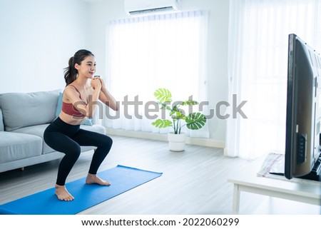 Asian Beautiful young woman stay home, doing aerobic exercise at home. Attractive girl doing lockdown activity, workout by squatting, follow instructions video from online trainer for health in house. Royalty-Free Stock Photo #2022060299
