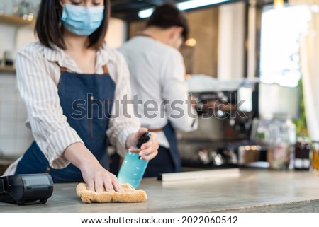 Cafe waiter wear mask, clean restaurant with sanitizer to open store. Asian attrctive young couple disinfecting, wiping and rubbing on counter in restaurant before reopen store after Covid19 lockdown. Royalty-Free Stock Photo #2022060542