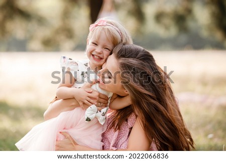 Young mother is playing with her little daughter in the park on summer day. Family holiday in garden. Portrait mom with child together on nature. Mum, little daughter outdoors. Happy Mothers Day.