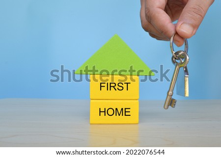 Hand holding key beside the home model with text FIRST HOME
