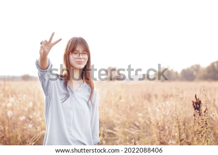 Teenage girl with glasses shows victory sign.