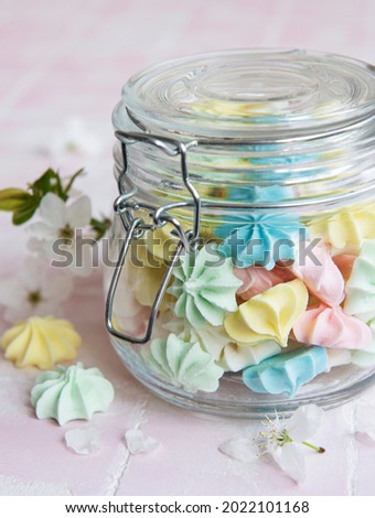 Small colorful meringues in the  glass jar on pink tile background
